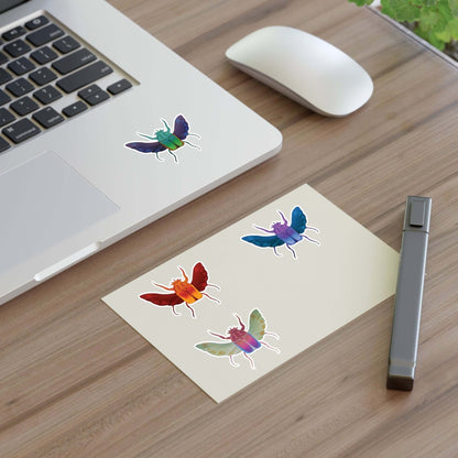 Die-cut insect stickers on two sheets on a desk near a laptop and pen.
