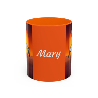 Orange coffee mug with “Mary” script and origami crane artwork on black side panels
