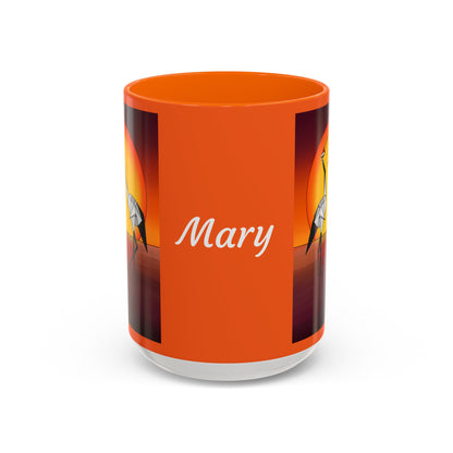 Orange coffee mug with orange lid, “Mary” script and origami crane graphic on sides