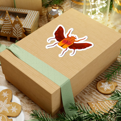 Beetle kiss-cut sticker centered on beige gift box with green ribbon, red wings and orange