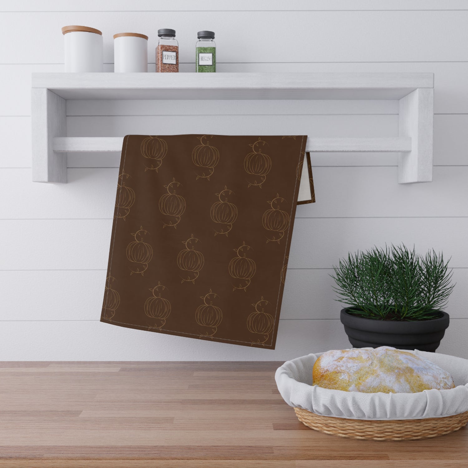 Brown tea towel with repeating pumpkin line pattern, folded and hanging