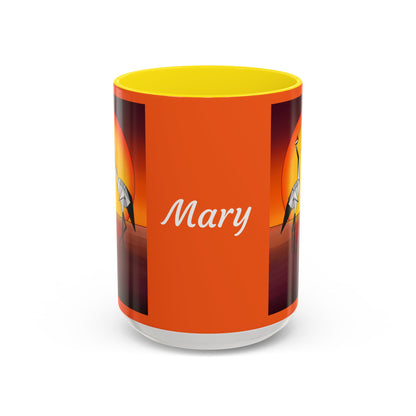 Orange coffee mug with yellow lid, “Mary” text and origami crane artwork on sides