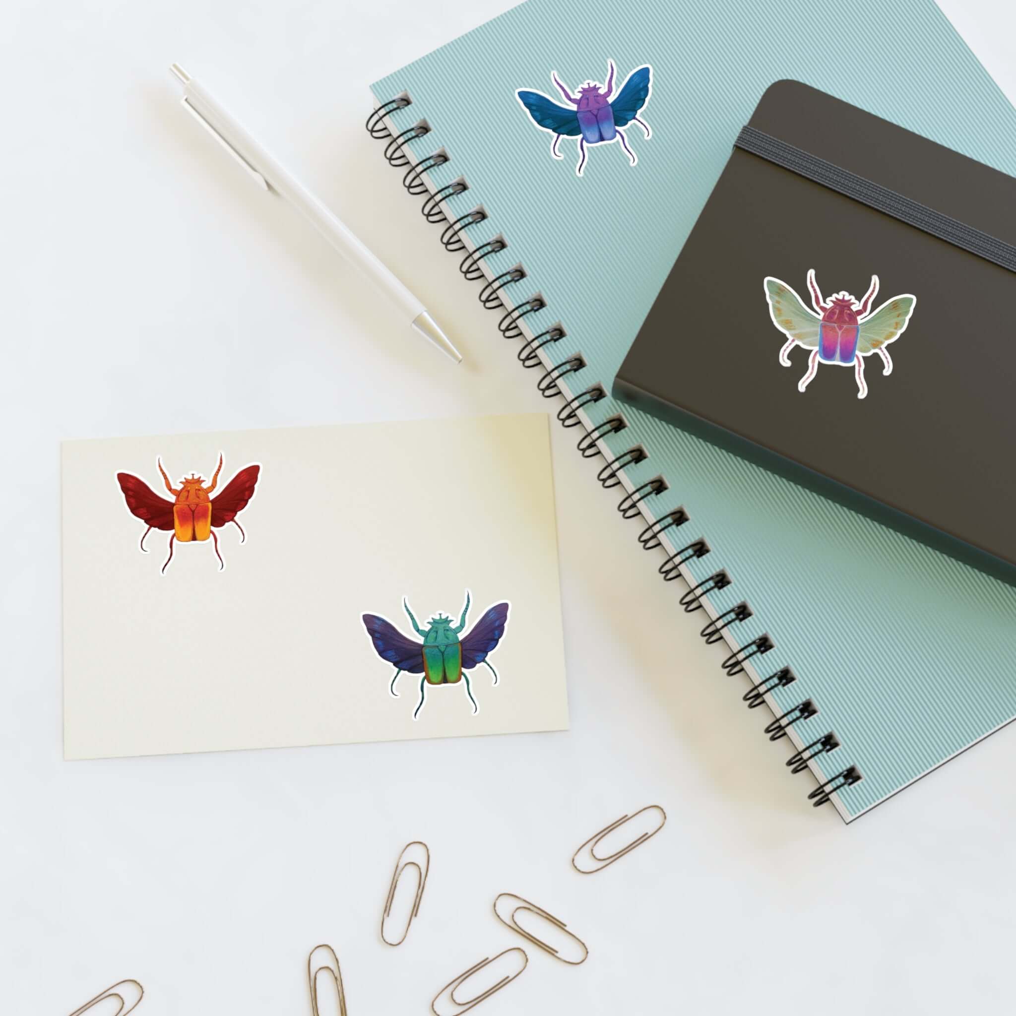 Small die-cut insect stickers on paper with a spiral notebook and a cover notebook.