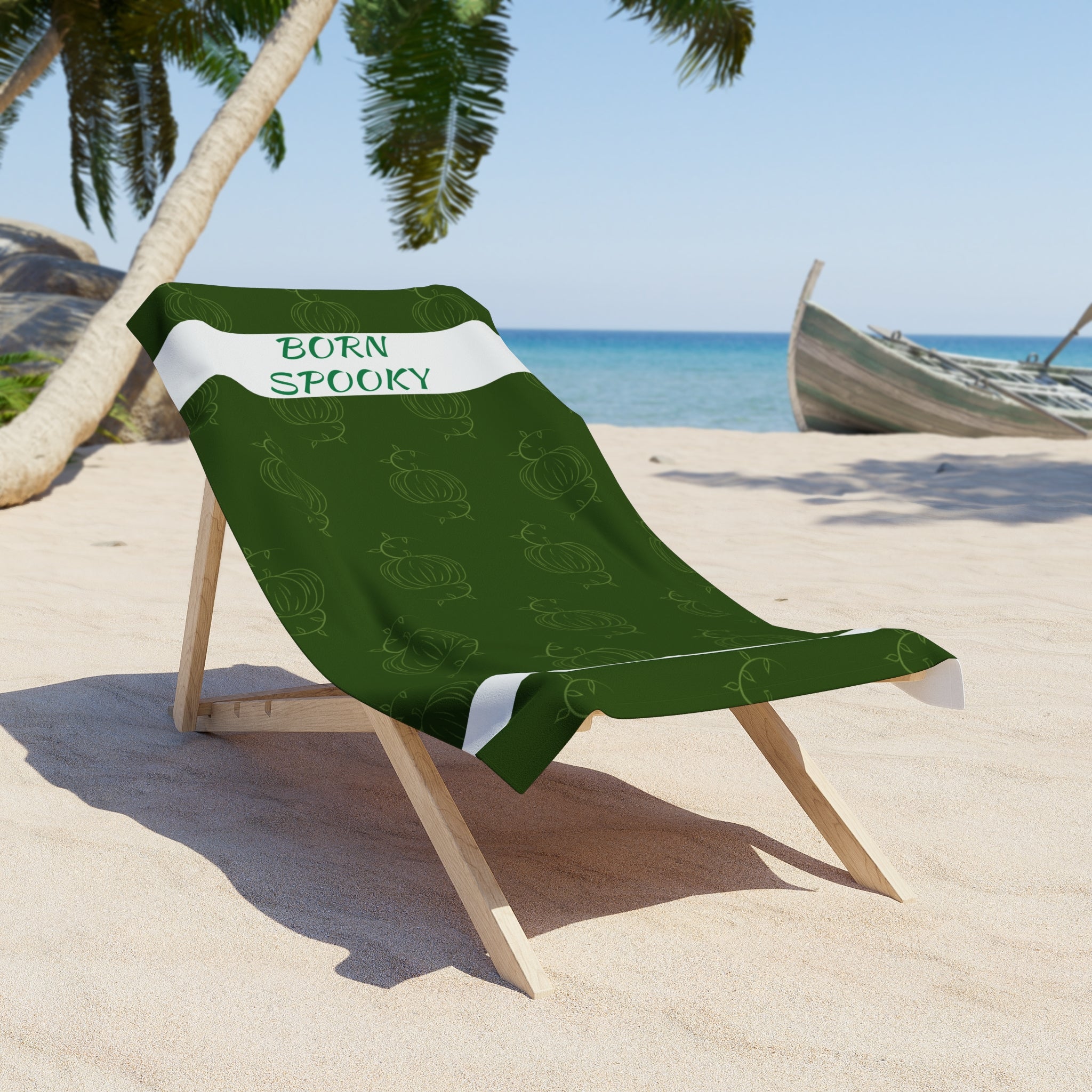 Green pumpkin beach towel with white stripe and “BORN SPOOKY” lettering, draped on chair
