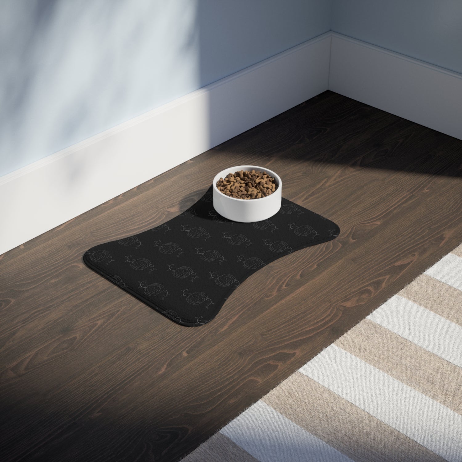 Black pet feeding mat with pumpkin pattern and centered white bowl of kibble