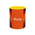 Orange coffee mug with yellow lid, “Mary” text and origami crane graphic on sides