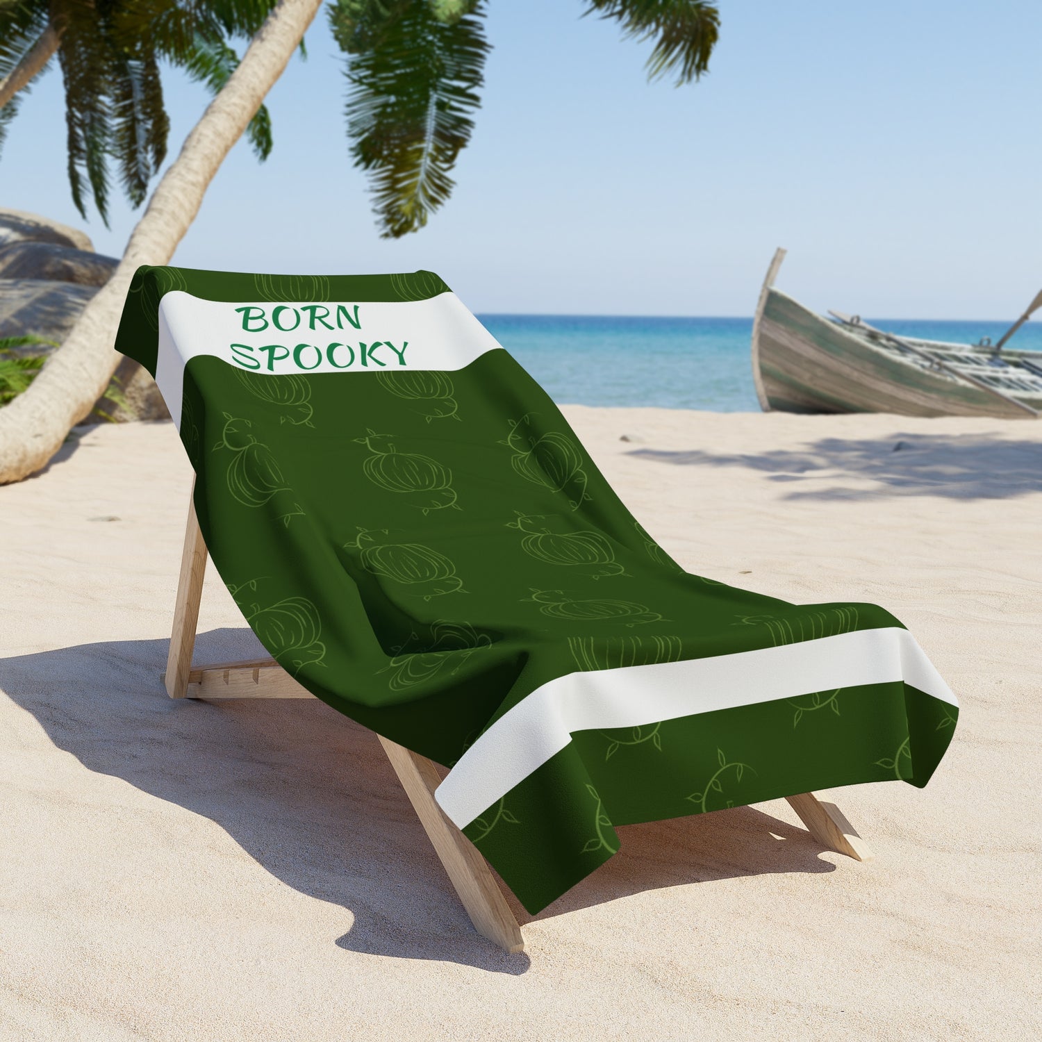 Green pumpkin-themed beach towel with “BORN SPOOKY” text, white accents, on lounge chair