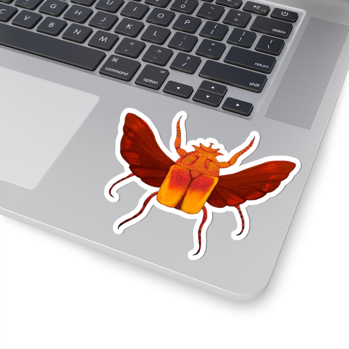 Beetle kiss-cut sticker on laptop trackpad: red wings, orange body, white outline
